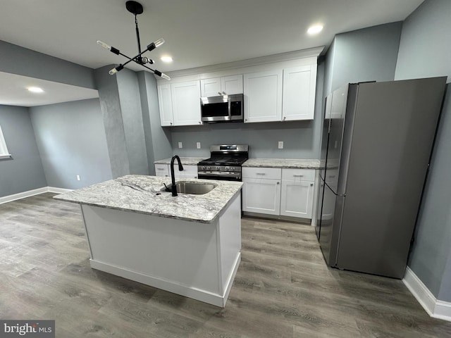 kitchen with stainless steel appliances, an island with sink, light stone counters, white cabinets, and sink