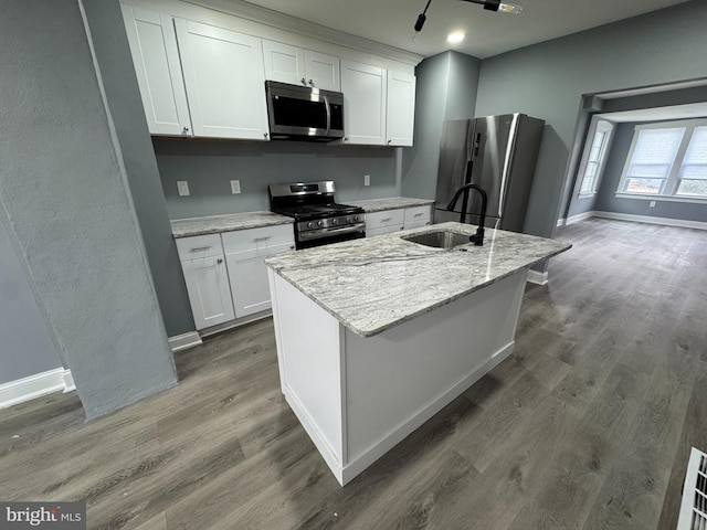 kitchen featuring appliances with stainless steel finishes, an island with sink, light stone countertops, white cabinets, and sink