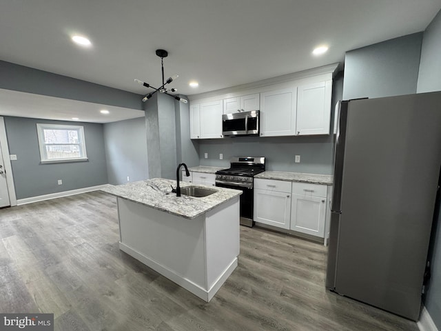 kitchen featuring sink, stainless steel appliances, white cabinets, hanging light fixtures, and a kitchen island with sink