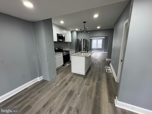 kitchen featuring appliances with stainless steel finishes, dark wood-type flooring, light stone countertops, white cabinets, and a kitchen island with sink