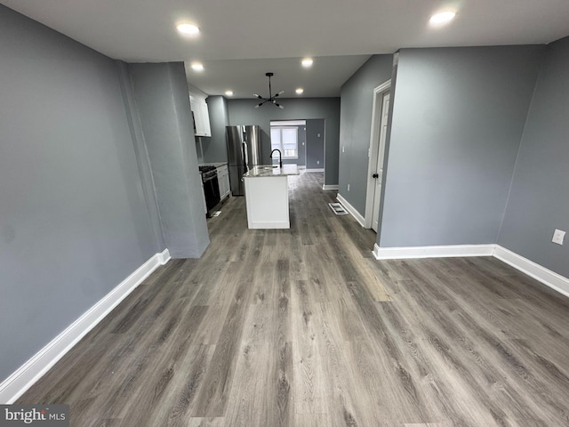 kitchen with stainless steel refrigerator, an island with sink, white cabinetry, and dark hardwood / wood-style flooring