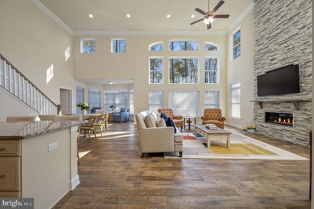 living room featuring a stone fireplace, ornamental molding, ceiling fan, and dark hardwood / wood-style flooring