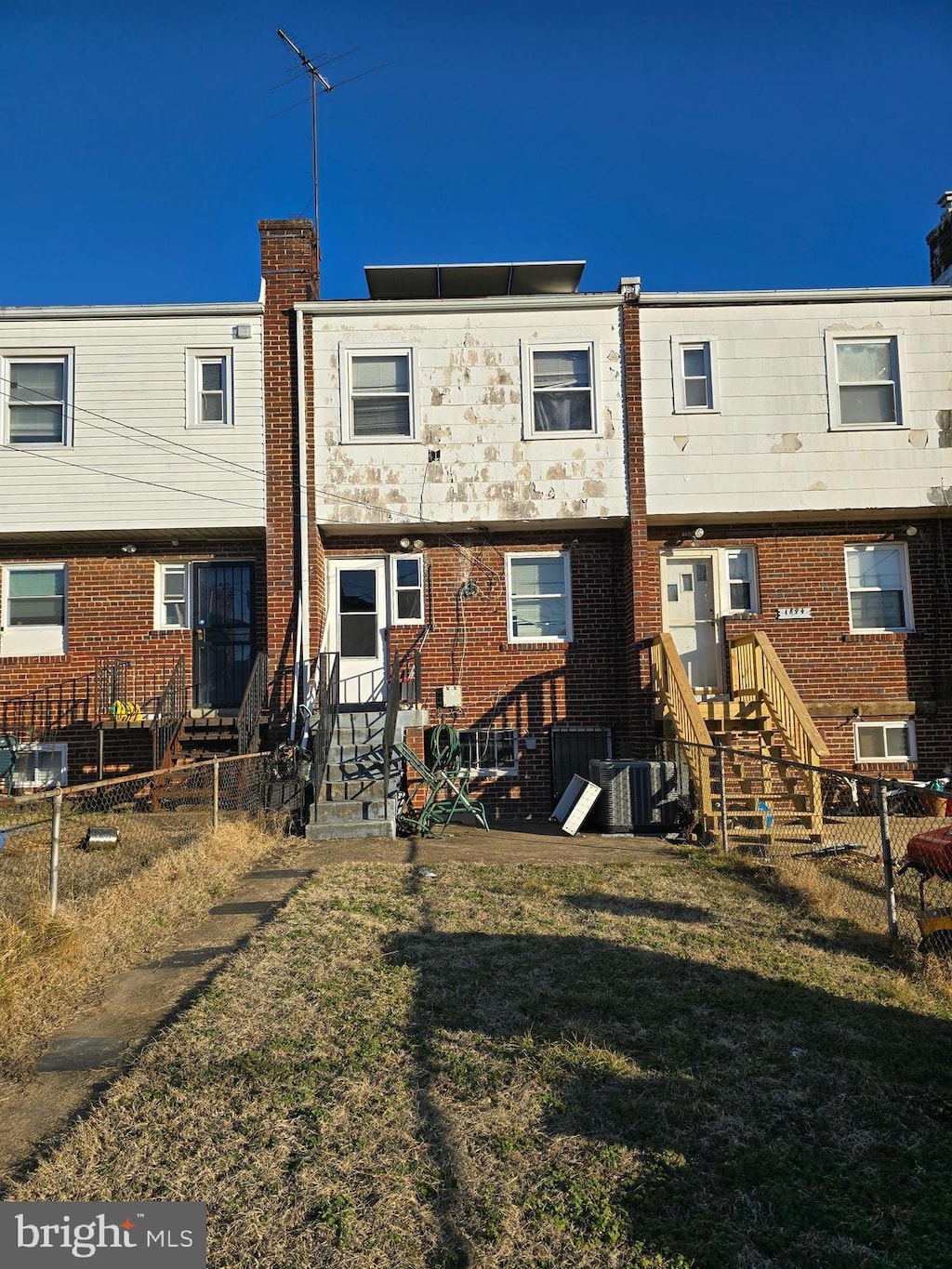 rear view of house with central AC unit and a yard