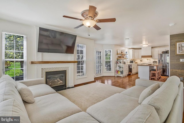 living area with a fireplace, wood finished floors, a wealth of natural light, and ceiling fan