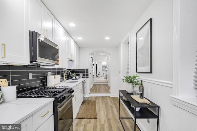 kitchen with appliances with stainless steel finishes, sink, white cabinetry, and light stone countertops