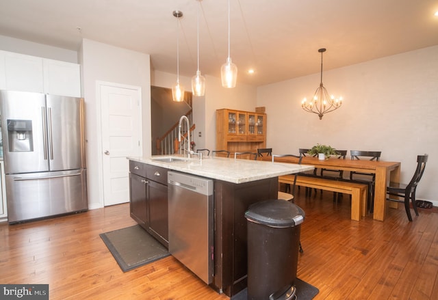 kitchen with light wood-style flooring, stainless steel appliances, a chandelier, pendant lighting, and a sink