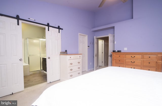 bedroom featuring light carpet, ceiling fan, ensuite bathroom, and a barn door