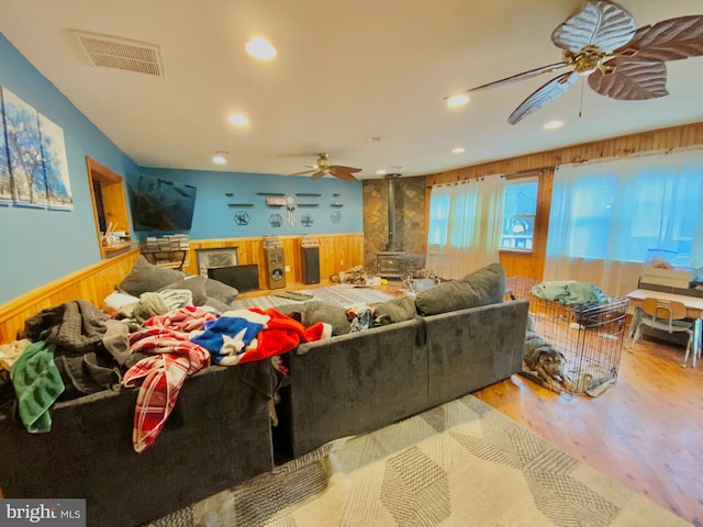 living room with light wood-type flooring, a wood stove, wood walls, and ceiling fan