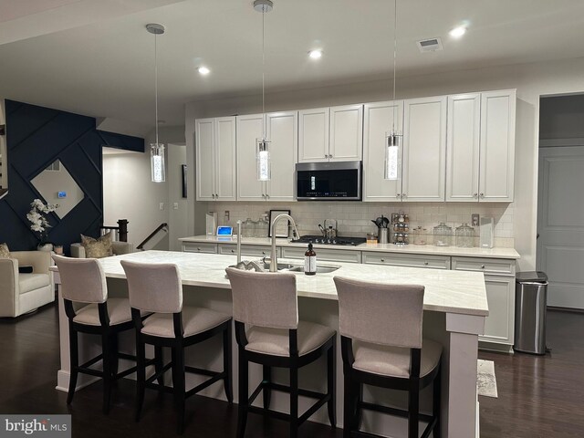 kitchen with stainless steel appliances, decorative light fixtures, a center island with sink, and white cabinetry