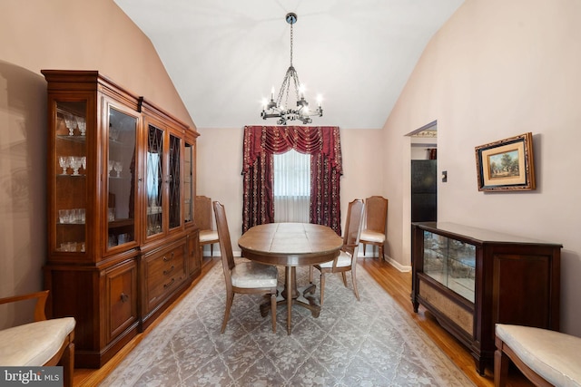 dining space featuring a chandelier, vaulted ceiling, baseboards, and wood finished floors