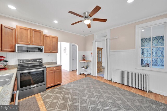 kitchen with ceiling fan, appliances with stainless steel finishes, arched walkways, wood finished floors, and radiator