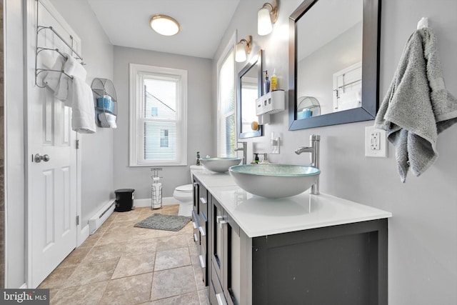 bathroom with double vanity, toilet, a sink, and a baseboard radiator