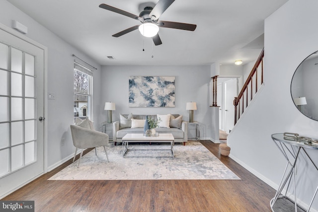 living room with dark wood-type flooring, a ceiling fan, visible vents, stairs, and baseboards