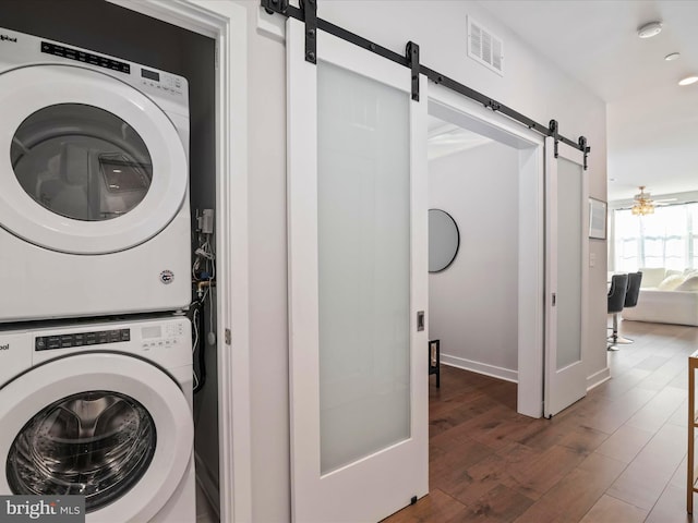 clothes washing area featuring a barn door, dark wood-type flooring, and stacked washer / drying machine