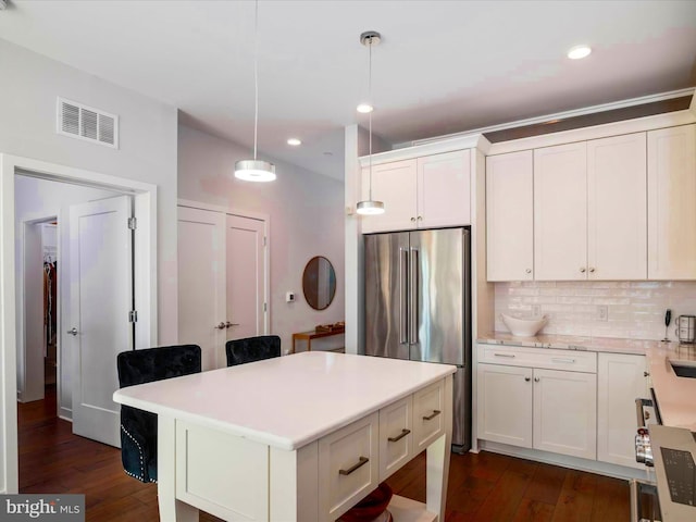 kitchen featuring hanging light fixtures, a breakfast bar, high end refrigerator, backsplash, and white cabinets