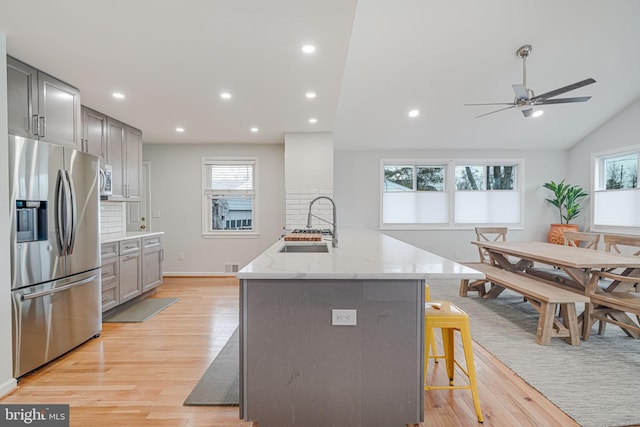 kitchen with an island with sink, stainless steel fridge with ice dispenser, sink, gray cabinets, and a breakfast bar area