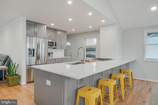 kitchen with a kitchen bar, sink, gray cabinetry, stainless steel appliances, and kitchen peninsula