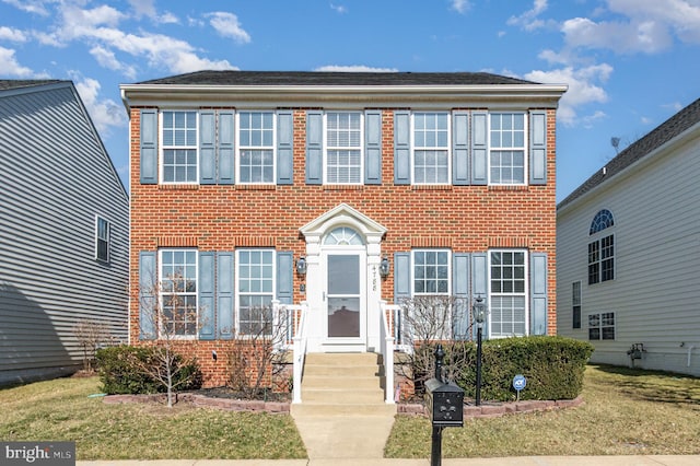 colonial home featuring entry steps, a front lawn, and brick siding