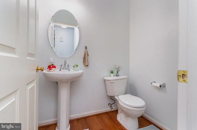 half bath featuring wood finished floors, toilet, and baseboards