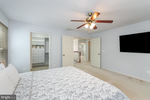 bedroom featuring a walk in closet, light colored carpet, visible vents, a ceiling fan, and baseboards