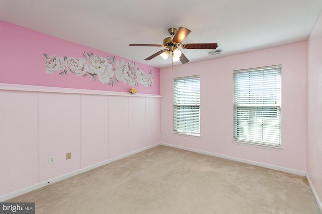 empty room featuring light carpet, ceiling fan, visible vents, and baseboards