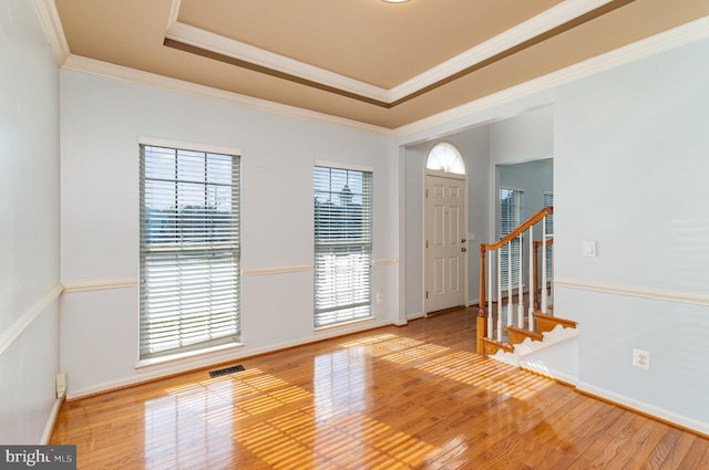 entryway featuring crown molding, a raised ceiling, visible vents, light wood-style flooring, and stairs