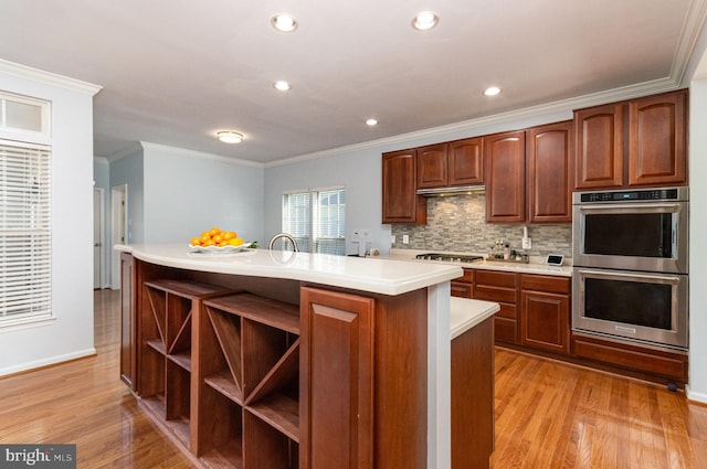 kitchen featuring light wood finished floors, a kitchen island with sink, light countertops, stainless steel double oven, and gas cooktop