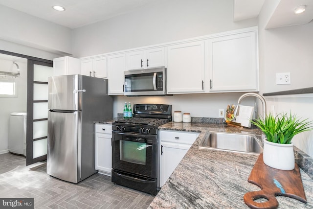 kitchen with washer / dryer, white cabinets, appliances with stainless steel finishes, dark stone countertops, and a sink