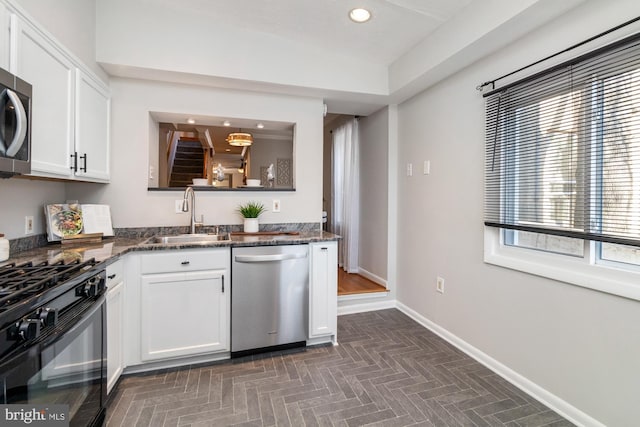 kitchen featuring appliances with stainless steel finishes, white cabinets, a sink, and dark stone counters