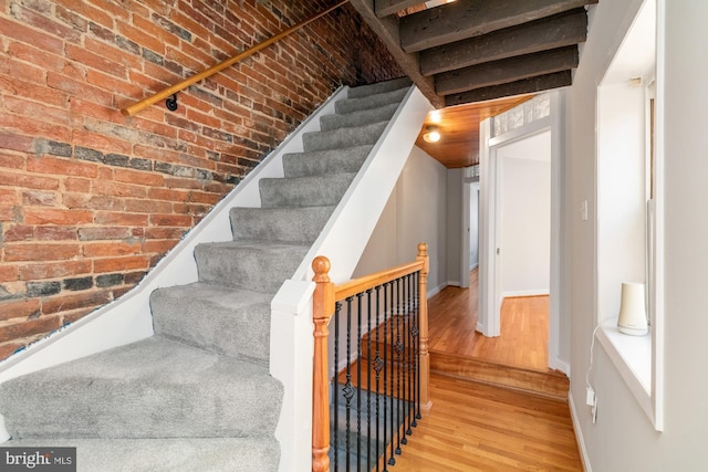 stairway featuring brick wall, baseboards, and wood finished floors