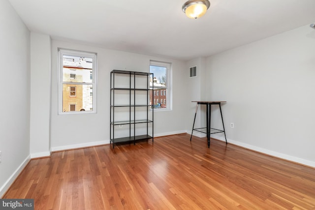 empty room with a wealth of natural light, baseboards, visible vents, and wood finished floors