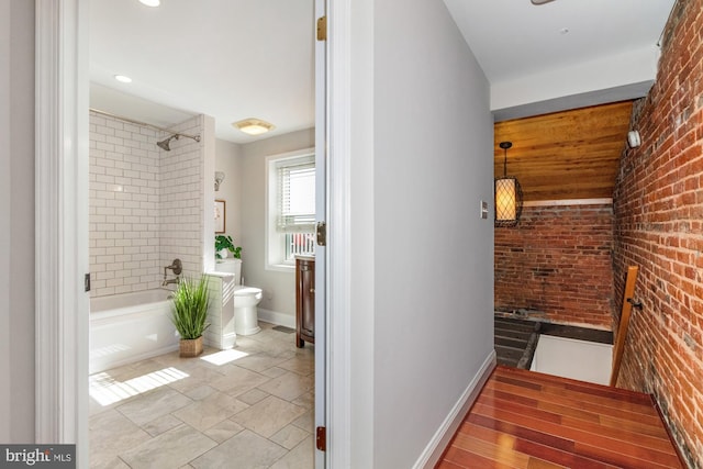 full bathroom with brick wall, bathing tub / shower combination, toilet, and baseboards