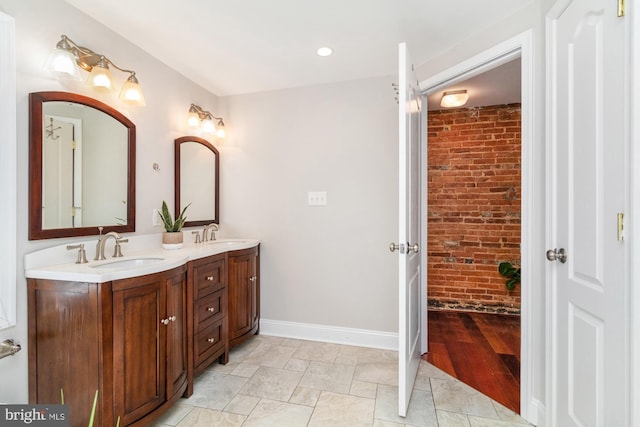 full bathroom with baseboards, a sink, brick wall, and double vanity