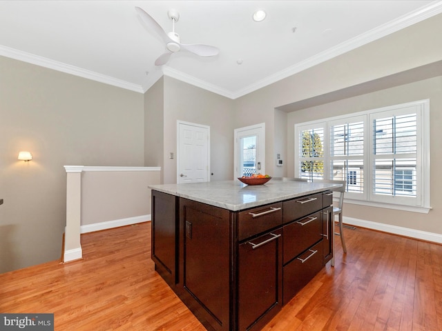 kitchen featuring dark brown cabinets, light stone countertops, light hardwood / wood-style floors, crown molding, and a center island