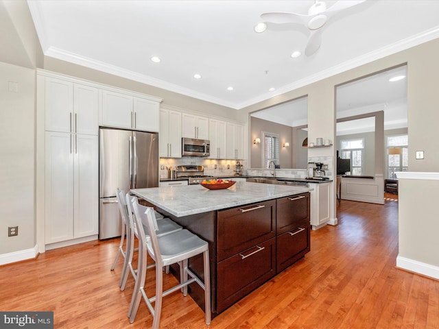 kitchen featuring white cabinetry, a center island, light stone countertops, appliances with stainless steel finishes, and a kitchen breakfast bar