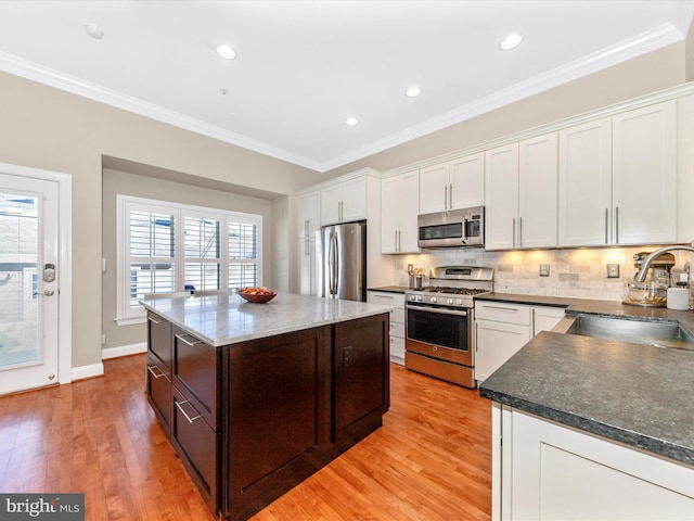 kitchen featuring sink, light wood-type flooring, white cabinetry, stainless steel appliances, and ornamental molding