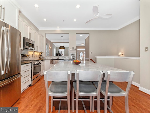 kitchen featuring white cabinetry, a kitchen bar, stainless steel appliances, and decorative light fixtures