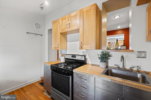 kitchen with light wood-style flooring, a sink, light countertops, light brown cabinetry, and gas range