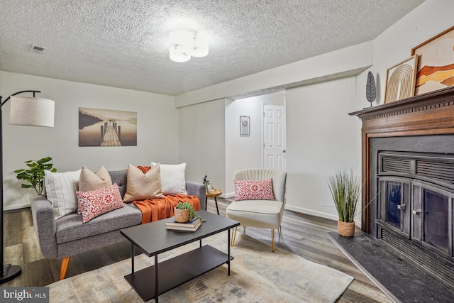 living room featuring a textured ceiling, wood finished floors, visible vents, baseboards, and a glass covered fireplace