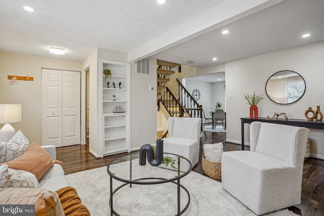 living area featuring wood finished floors, visible vents, a textured ceiling, and stairs