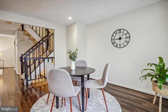 dining area with dark wood-type flooring, a textured ceiling, baseboards, and stairs