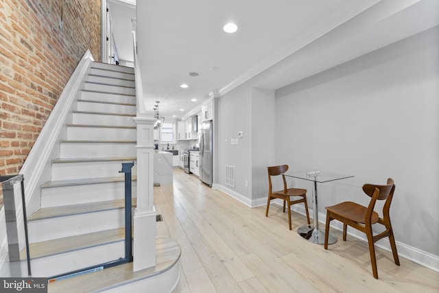 stairs with brick wall, wood finished floors, visible vents, and baseboards