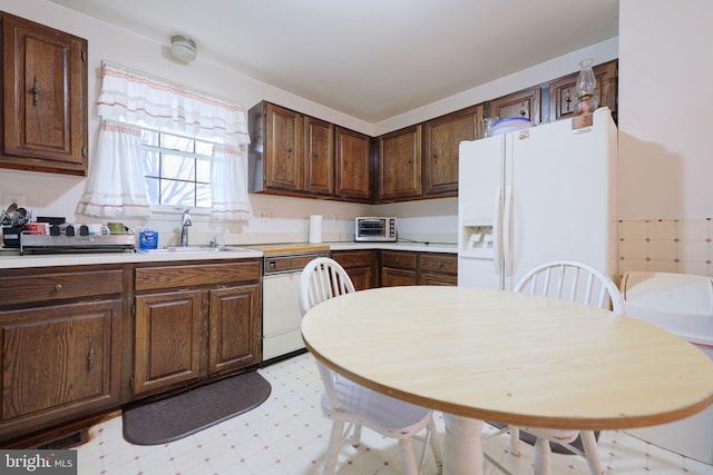 kitchen with white appliances, a sink, light countertops, dark brown cabinets, and light floors