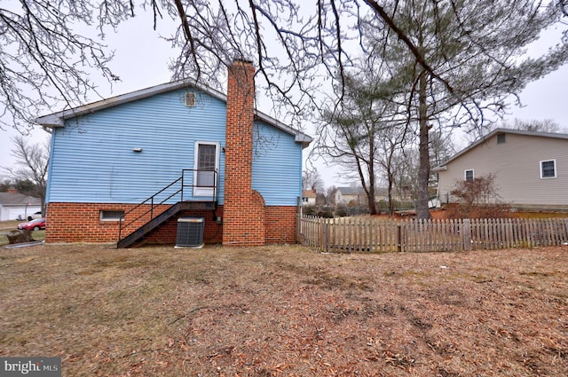 back of house with central AC, fence, and a chimney