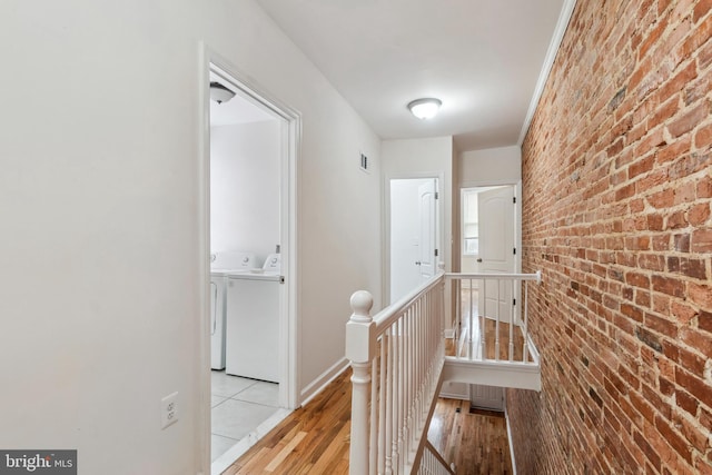 corridor with visible vents, light wood-style floors, brick wall, an upstairs landing, and washer and dryer