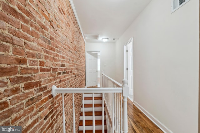 hallway featuring visible vents, baseboards, brick wall, wood finished floors, and an upstairs landing