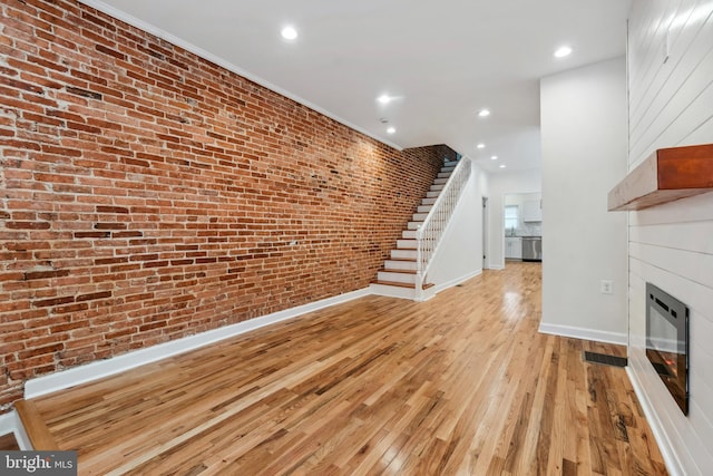 unfurnished living room featuring recessed lighting, light wood-style floors, a large fireplace, brick wall, and baseboards