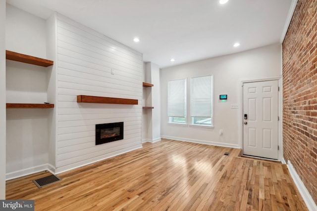 unfurnished living room featuring a large fireplace, light wood finished floors, visible vents, baseboards, and brick wall