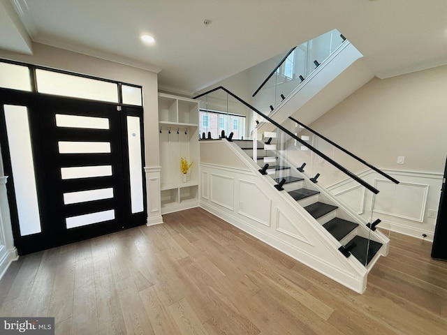 foyer with a wainscoted wall, crown molding, a decorative wall, stairway, and wood finished floors