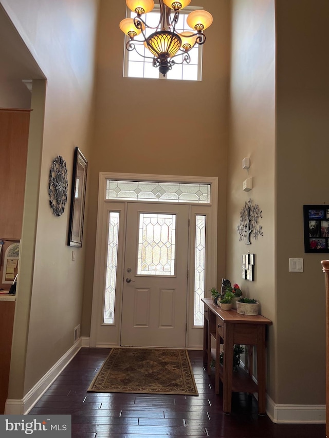 entrance foyer with dark wood-style floors, a notable chandelier, a towering ceiling, and baseboards